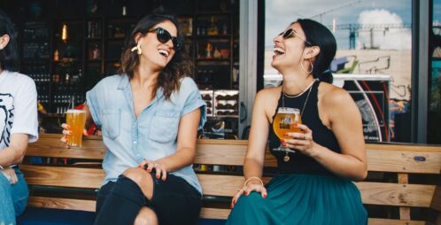 women laughing with beers in hand